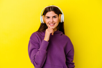 Young caucasian woman listening to music with headphones isolated on pink background smiling happy and confident, touching chin with hand.