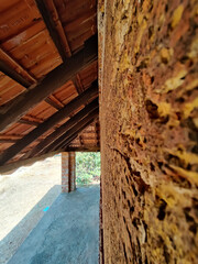 A buildings walls made out of red laterite rocks covered with clay tile roof