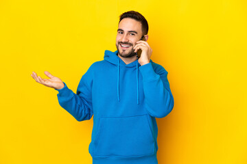 Young caucasian handsome man isolated on yellow background keeping a conversation with the mobile...