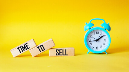 Time to Sell text on wooden blocks over yellow background with alarm clock