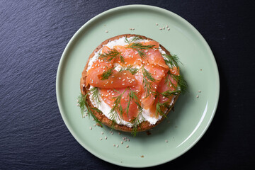 half a bun, oiled with fresh cream, garnished with smoked fish and sprinkled with fresh dill and sesame seeds on a plate