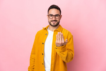 Young caucasian handsome man isolated on pink background inviting to come with hand. Happy that you came