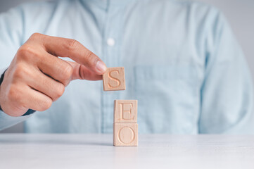 Businessmen wear a white shirt at their desks in the office. Use your hand to pick up a wooden cube inscribed with the word SEO.