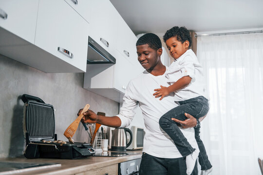 African american father with his son is indoors at home preparing mushrooms at kitchen