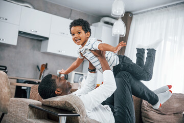 African american father with his son is indoors at home lying on the bed and having fun