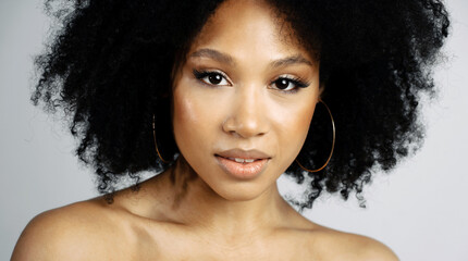 Beauty Portrait of a young female model of Afro-appearance posing. Healthy, Clean, Smooth facial skin. Working in a photo studio on a white background. Black healthy curly hair.