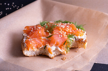 an appetizing, bitten off bun, greased with fresh cream, garnished with smoked fish trout and sprinkled with fresh dill and sesame seeds