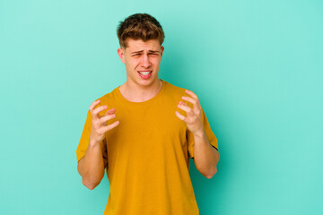 Young caucasian man isolated on blue background upset screaming with tense hands.