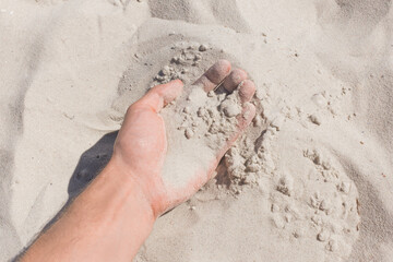 The guy's hand takes or touches the white beach sand close up