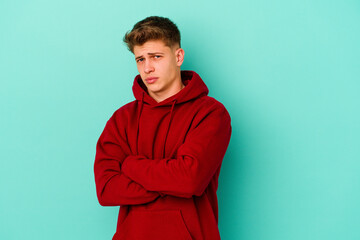 Young caucasian man isolated on blue background suspicious, uncertain, examining you.