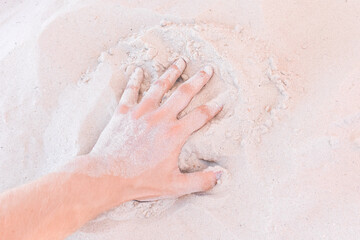 The guy's hand takes or touches the white beach sand close up