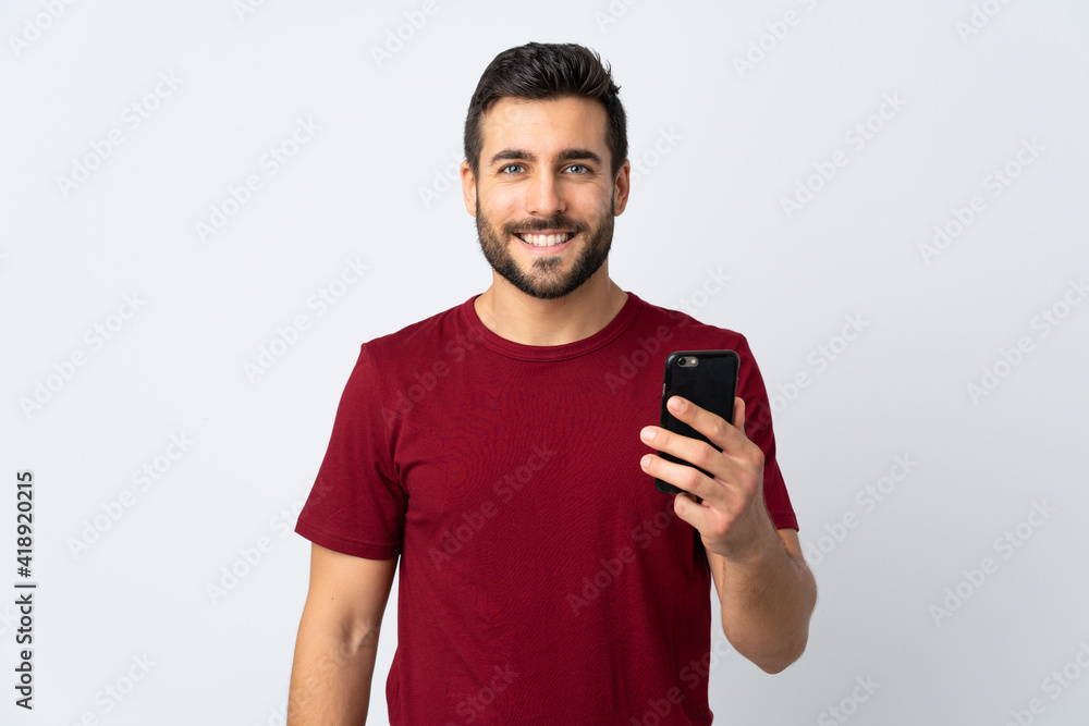 Canvas Prints Young handsome man with beard using mobile phone isolated on white background smiling a lot