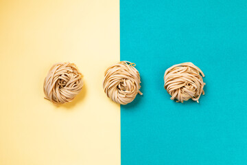 Fettuccine : 3 nest of raw pasta on divided background yellow and light blue. Simple composition about italian quality pasta. 