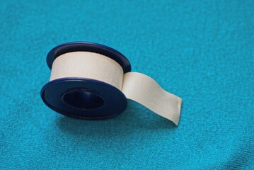 one round plastic spool with a white medical tape stands on a blue cloth