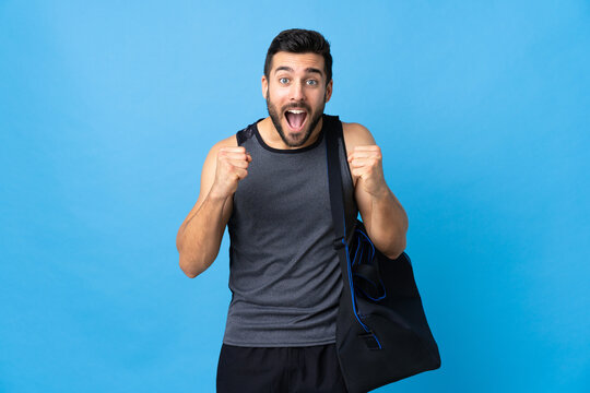 Young Sport Man With Sport Bag Isolated On Blue Background Celebrating A Victory In Winner Position