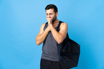 Young sport man with sport bag isolated on blue background coughing a lot