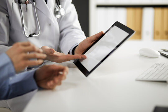 Unknown male doctor and patient woman discussing current health examination while sitting in clinic and using tablet computer, closeup of hands. Medicine and healthcare concept