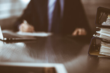 Binders with papers are waiting to be processed by man accountant in blue blazer staying at home during covid pandemic. Taxes and audit concept. Internal Revenue Service inspector checking financial