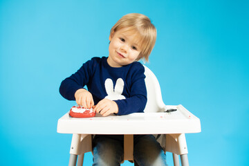Little baby boy is eating donuts isolated over blue background. Tasty food for kids.