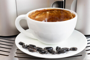 Brewing fresh coffee from your espresso machine. Budget coffee maker. White cup decorated with coffee beans.