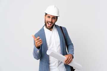 Young architect man with helmet and holding blueprints isolated on white background pointing to the front and smiling