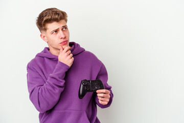 Young caucasian man holding a gamepad isolated on white background looking sideways with doubtful and skeptical expression.