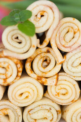 Traditional Russian blini or pancakes for Maslenitsa or pancake week wrapped in rolls and stacked in a pyramid and pink tulips