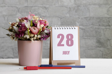 july 28. 28th day of the month, calendar date.A delicate bouquet of flowers in a pink vase, two pencils and a calendar with a date for the day on a wooden surface