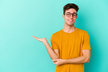 Young caucasian man isolated on blue background showing a copy space on a palm and holding another...