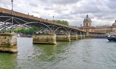 People walking on Pont des Arts bridge on the Seine river with Institut de France in background