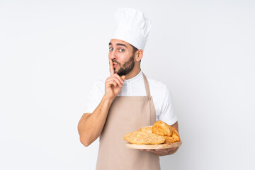 Male baker holding a table with several breads isolated on white background doing silence gesture