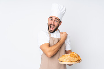 Male baker holding a table with several breads isolated on white background celebrating a victory