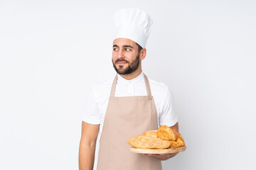 Male baker holding a table with several breads isolated on white background standing and looking to the side