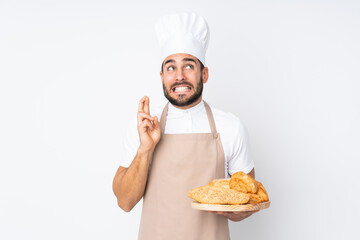 Male baker holding a table with several breads isolated on white background with fingers crossing
