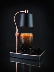 Fototapeta na wymiar The luxury lighting aromatic scent glass candle is put on the electric lamp candle warmer heater on the black table to creat relax and romantic ambience on Valentine day