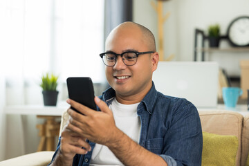 Young asian man Sit and relax in the living room on the sofa.He using texting smartphone and smile.