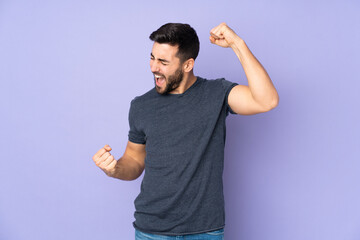 Caucasian handsome man celebrating a victory over isolated purple background