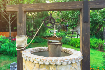 Beautiful artesian well made by stones and wheel pulley with metal bucket and rope in peaceful...
