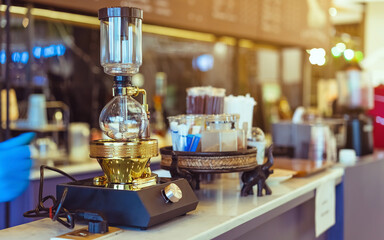 Close up to barista make coffee with Vacuum Pot Syphon Brewer.  Syphon (Siphon) coffee maker brews drink using two chambers where vapor pressure and vacuum produce coffee in cafe. Selective focus.