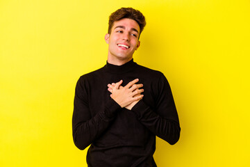 Young caucasian man isolated on yellow background laughing keeping hands on heart, concept of happiness.