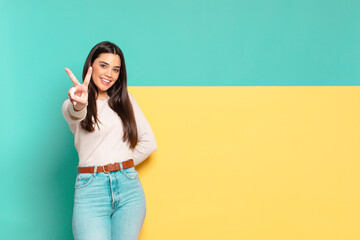 young pretty woman smiling and looking happy, carefree and positive, gesturing victory or peace...