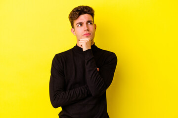 Young caucasian man isolated on yellow background thinking and looking up, being reflective, contemplating, having a fantasy.