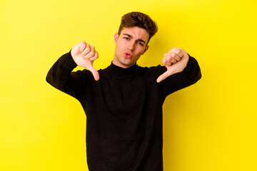 Young caucasian man isolated on yellow background showing thumb down and expressing dislike.