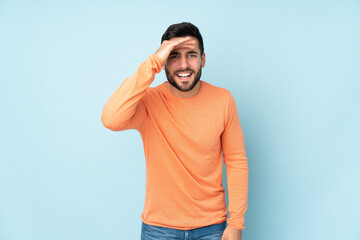 Fototapeta premium Caucasian handsome man looking far away with hand to look something over isolated blue background