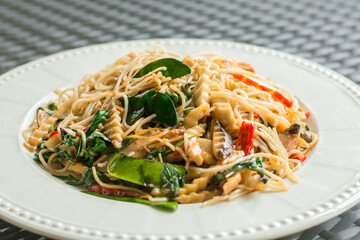 Vegan food concept. Stir-fried hot and spicy noodles with mushroom, chili, and sweet basil on a white plate in a restaurant.