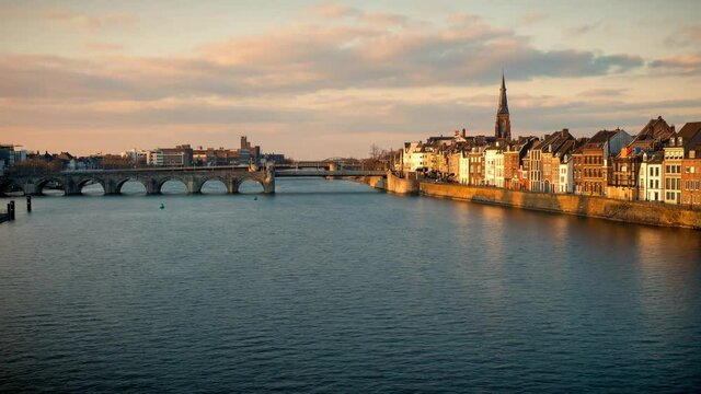 Time lapse view of a beautiful sunset at the waterfront of Maastricht, the Netherlands, with people walking along the promenade in front of old town houses at the river Maas
