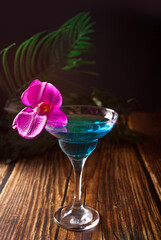 Summer tropical blue cocktail decorated purple orchid flower on the wooden background