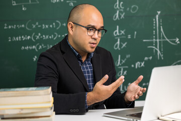 Indian young teacher man sitting teaching online video conference live stream by laptop. Asian teacher teaching mathematics class webinar online for students learning.