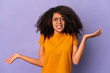 Young african american curly woman isolated on purple background confused and doubtful shrugging shoulders to hold a copy space.