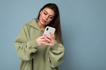 Photo of serious Beautiful young brunette woman wearing stylish green hoodie using mobile phone...